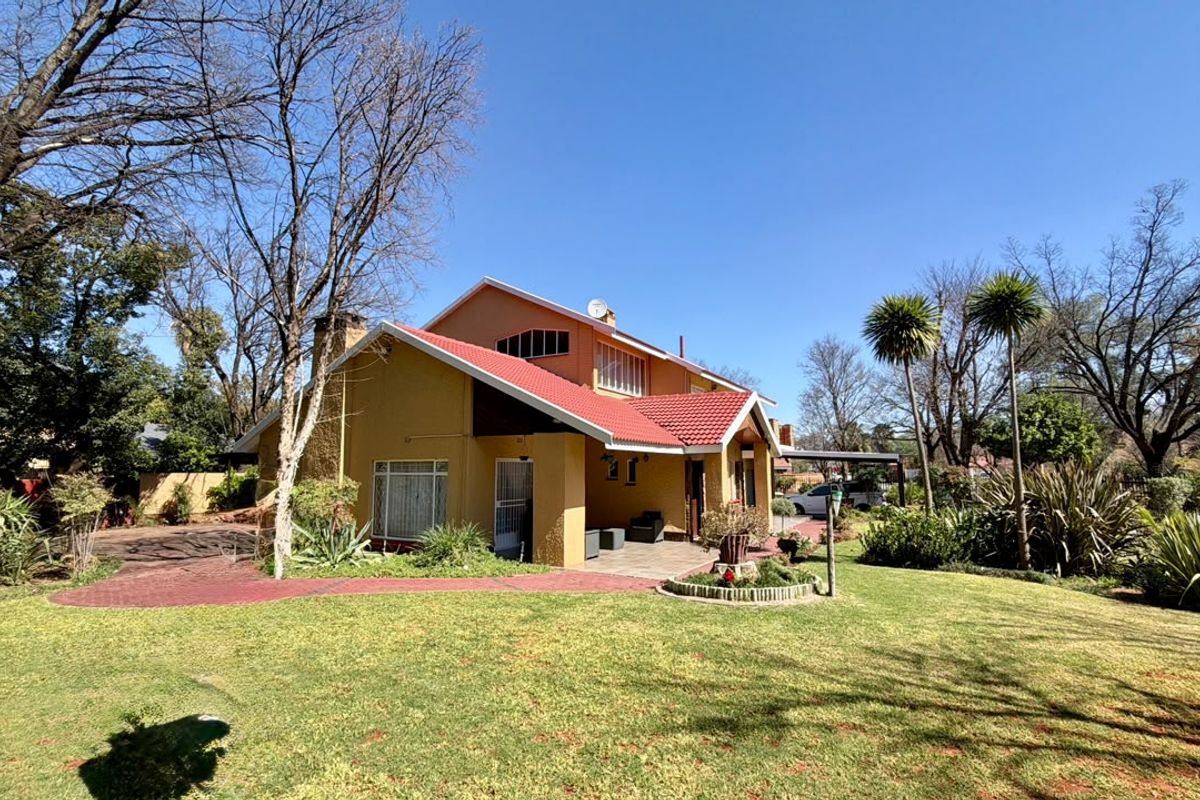 A view of the rear elevation of the house featuring a red tiled roof, covered patio area, and a well-maintained garden.