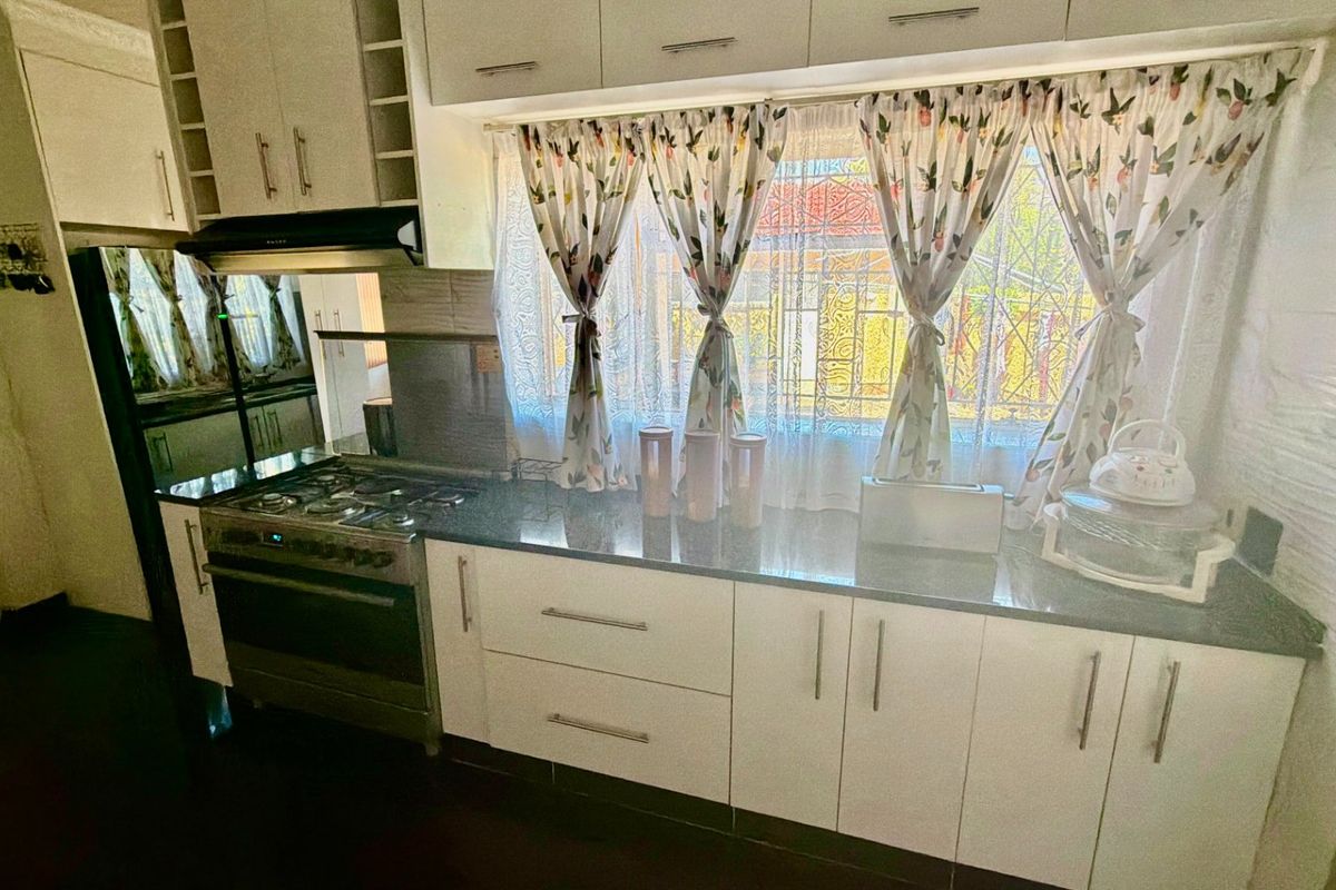A functional kitchen featuring white built-in cabinetry, dark granite countertops, a gas stove with an extractor fan, and a window overlooking the exterior.