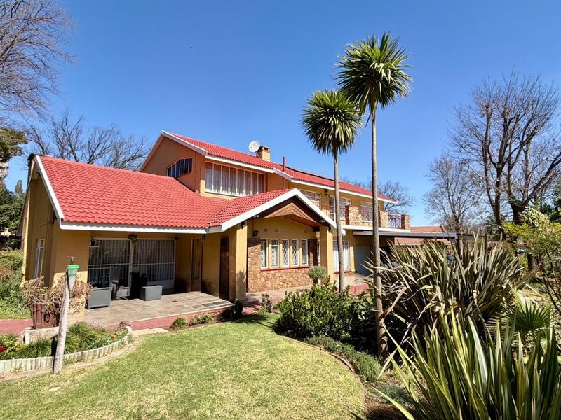 A well-maintained double-story house featuring a distinctive red tiled roof, stone facade accents, and a landscaped front garden with a paved patio area.