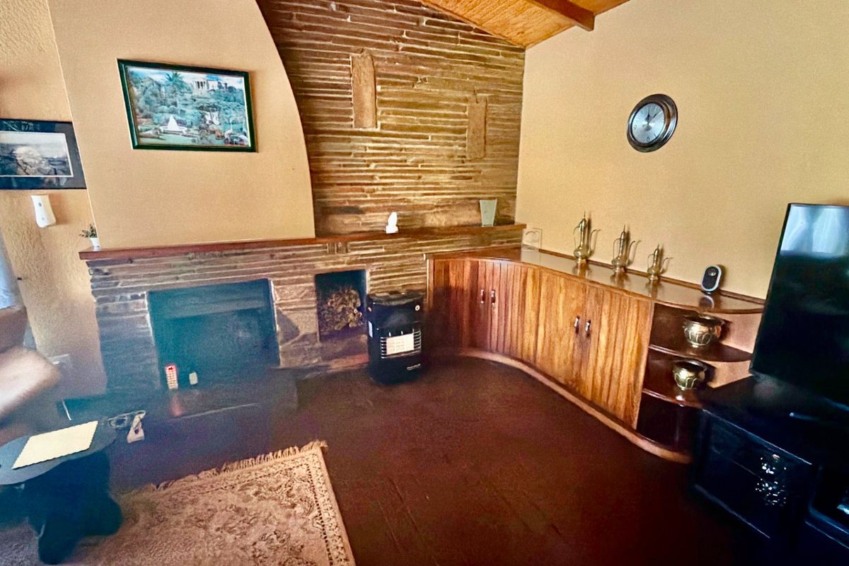 Living room featuring a stone fireplace, built-in curved wooden cabinetry, and exposed timber ceiling beams, offering a rustic and traditional aesthetic.