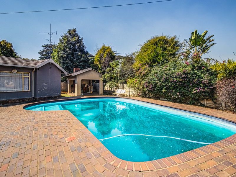 A backyard pool area featuring a swimming pool with brick paving surround and a small covered outdoor structure.