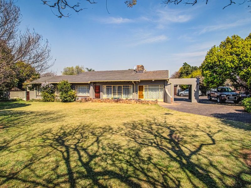 A single-story residential home featuring a tiled roof, stone retaining wall, and a paved driveway with an attached carport, set on a large lawn.