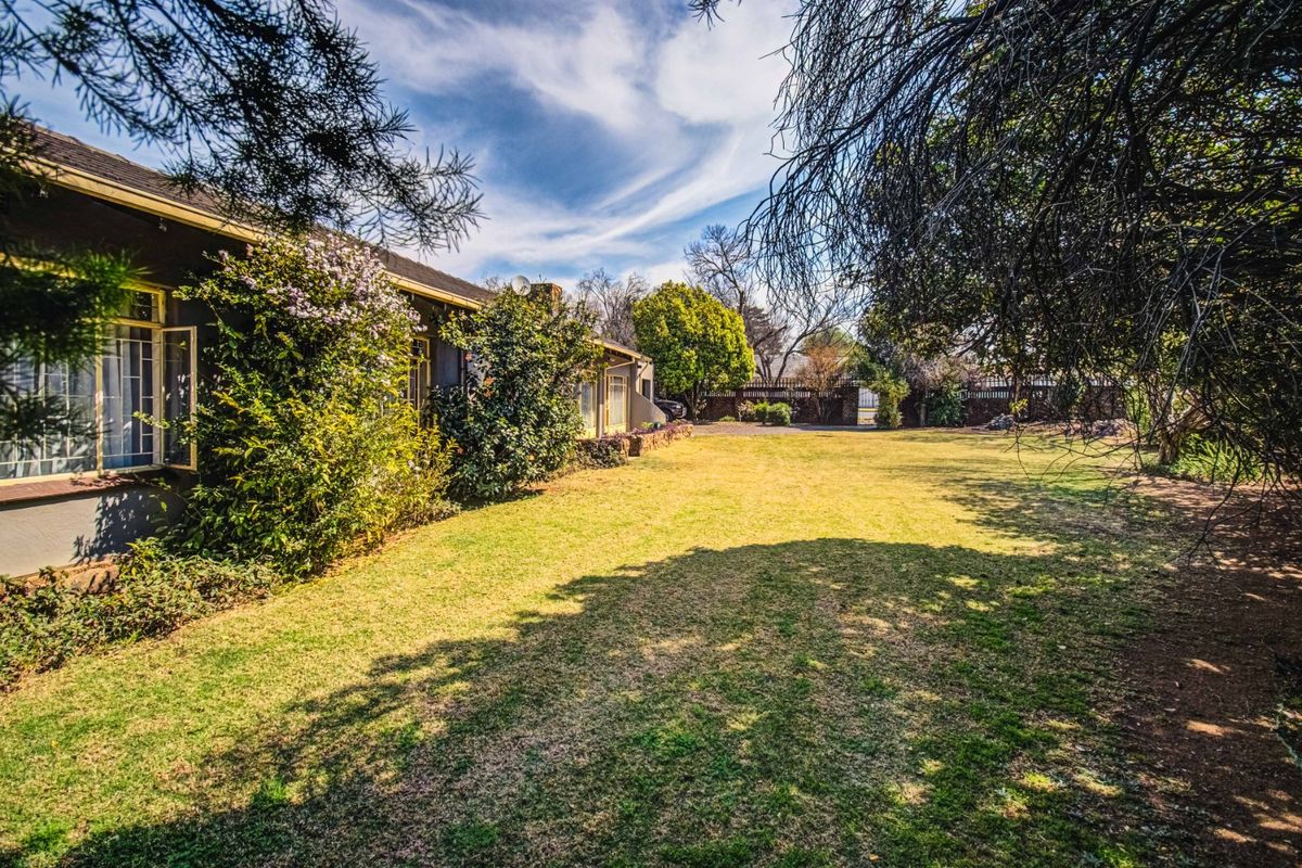 A spacious rear garden featuring a large lawn area, established trees, and a view of the property's rear facade with tiled roofing.