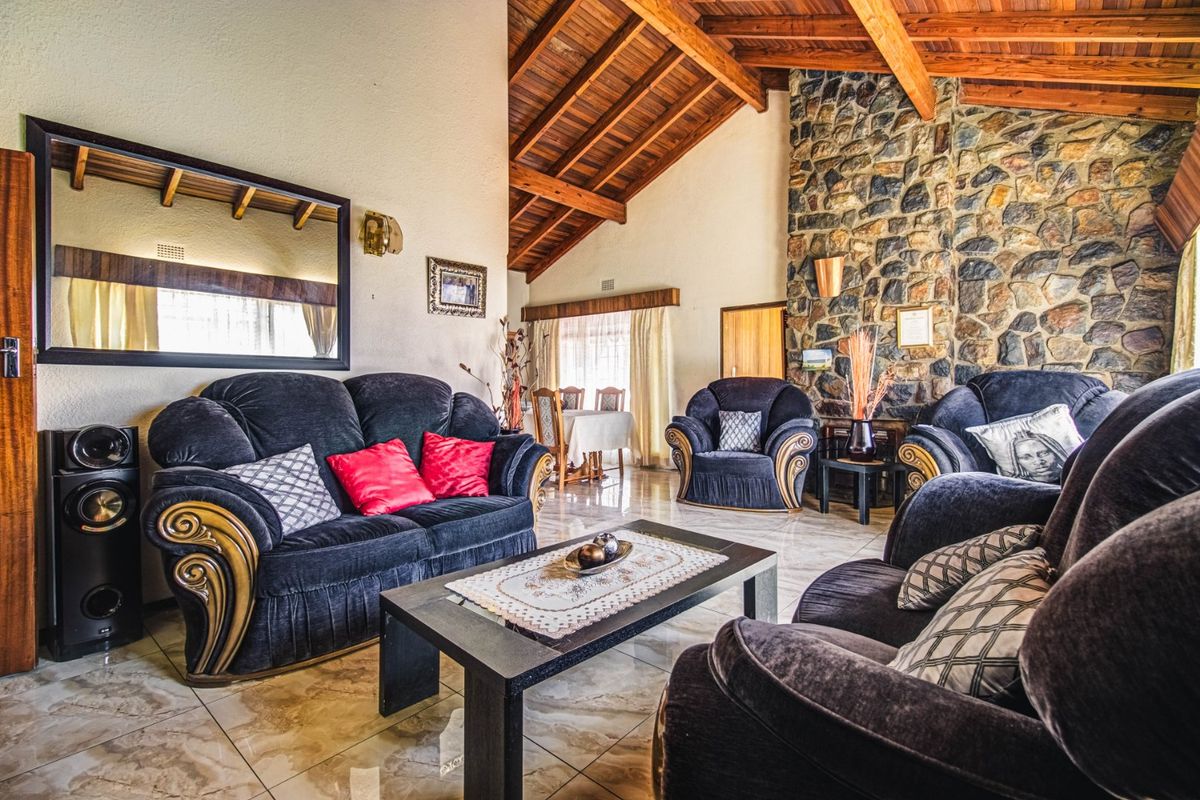 Spacious living room featuring a striking stone fireplace, high vaulted ceilings with exposed timber beams, and polished tiled flooring.