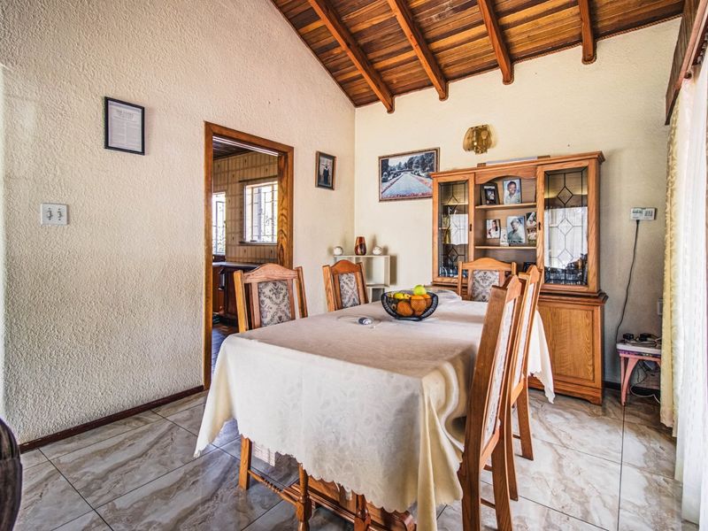 Dining room featuring exposed timber beam ceilings, textured walls, and tiled flooring, with an open doorway leading to the kitchen area.