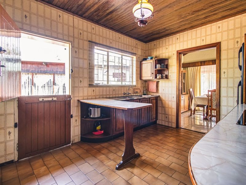 A dated kitchen featuring wooden cabinetry, tiled splashbacks, and a breakfast bar, with direct access to the exterior via a stable door.