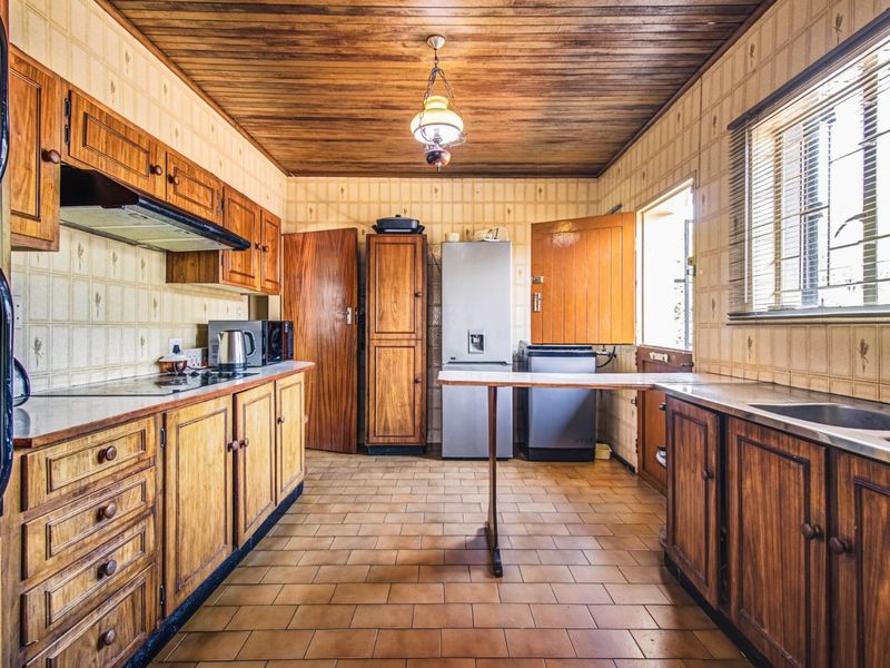 A dated kitchen featuring wooden cabinetry, tiled flooring, and a timber ceiling, offering a functional layout with potential for modern renovation.
