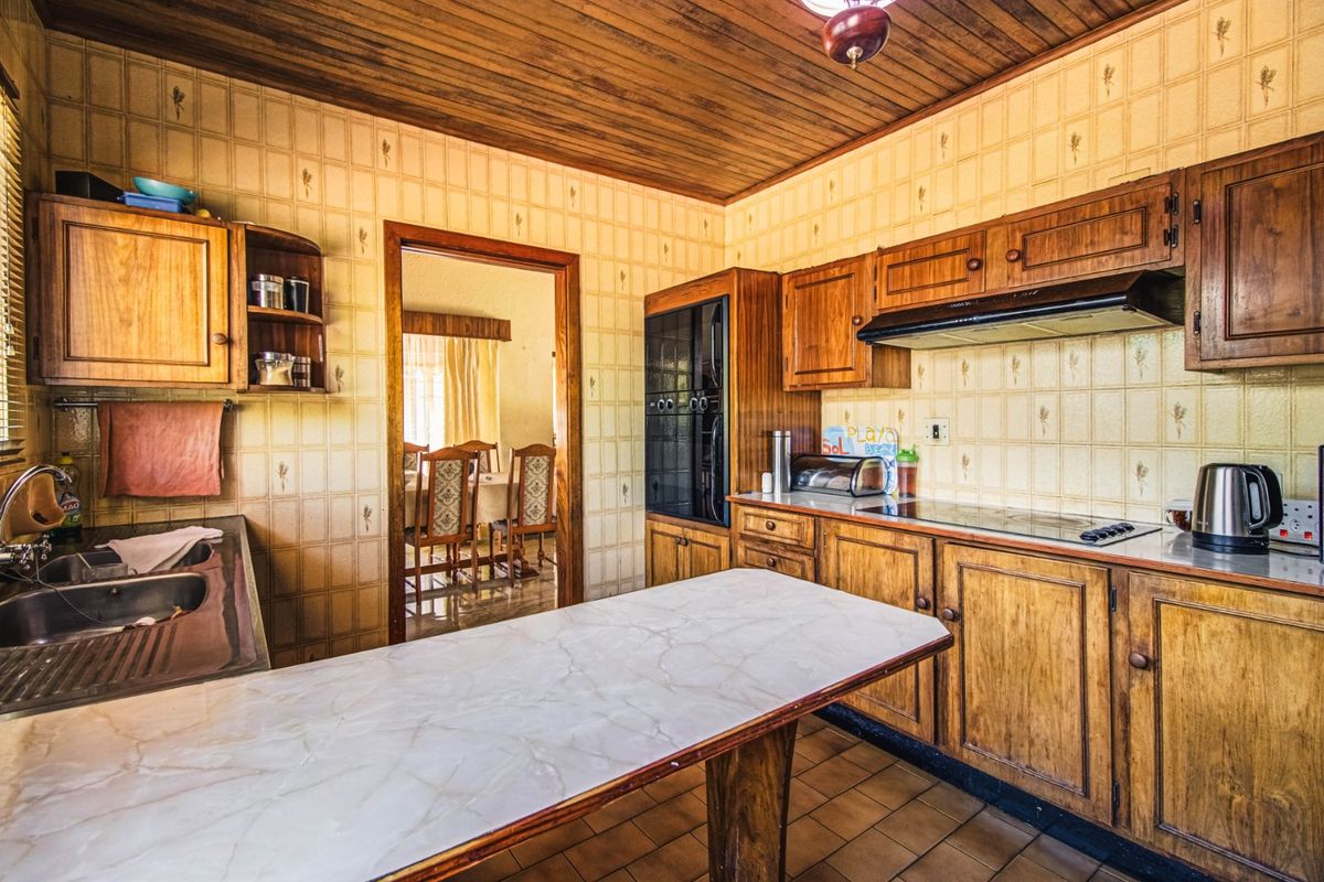 A dated kitchen featuring wooden cabinetry, a built-in oven, extractor fan, and tiled finishes, offering significant potential for a modern renovation.
