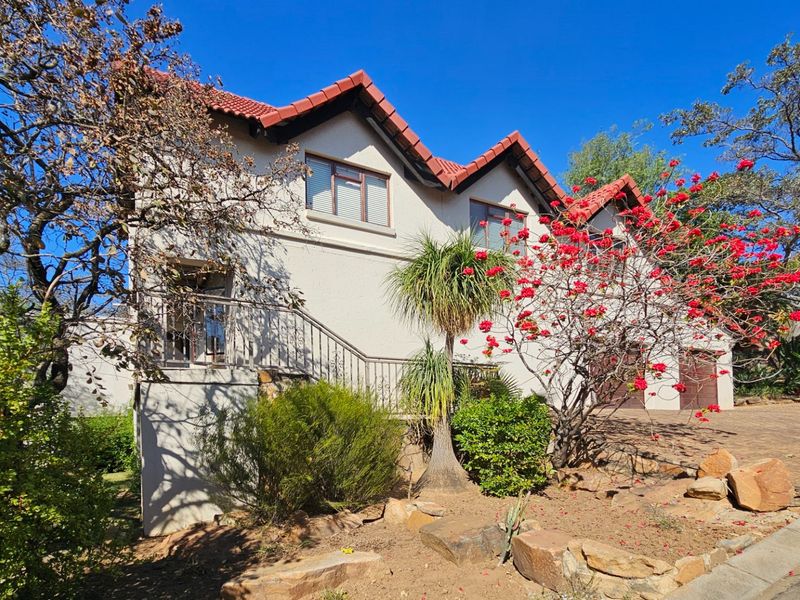 Front elevation of a multi-level house featuring a tiled roof, stucco exterior, metal staircase, and paved driveway with integrated garage access.