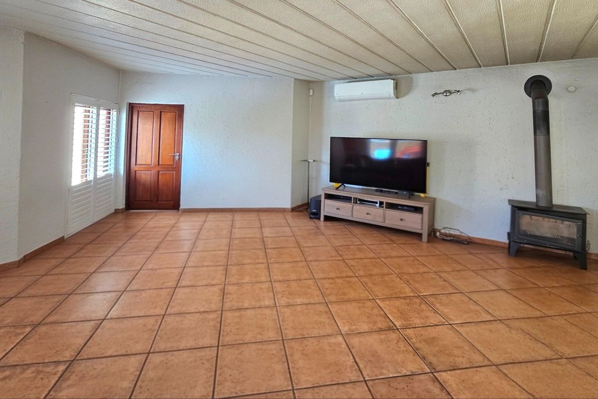 Spacious living room featuring terracotta-style floor tiles, a built-in wood-burning fireplace, and a wall-mounted air conditioning unit.