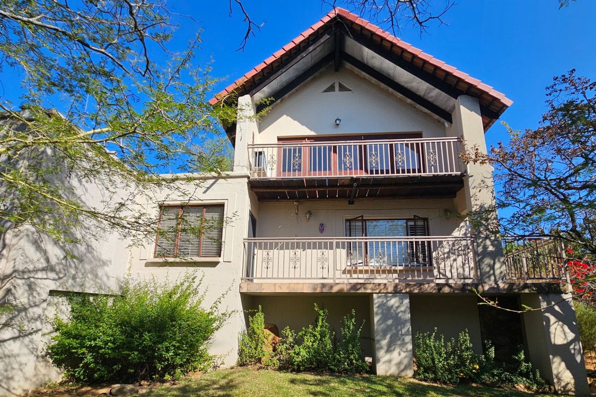 Rear elevation of a multi-story house featuring a tiled roof, two levels of balconies with wrought iron railings, and established garden surroundings.
