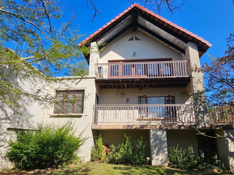 Rear elevation of a multi-story house featuring a tiled roof, two levels of balconies with wrought iron railings, and established garden surroundings.