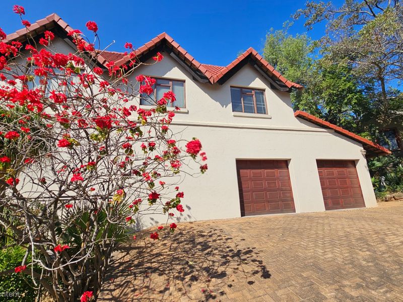Front elevation of a residential property featuring a double garage, tiled roof, and a paved driveway surrounded by established garden landscaping.