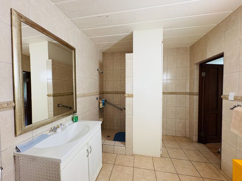 A functional bathroom featuring a vanity unit, walk-in shower with grab rail, and neutral ceramic tiling throughout.