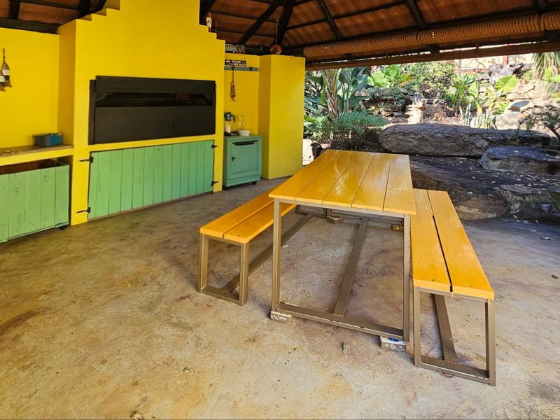 Covered outdoor patio area featuring a built-in braai, thatched roof, and concrete flooring, ideal for alfresco dining and entertaining.