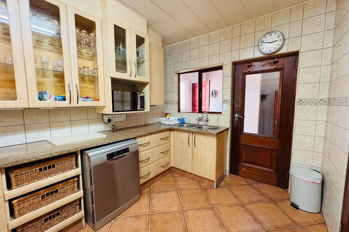 A functional kitchen featuring light wood cabinetry, granite countertops, a double basin sink, and tiled finishes throughout.
