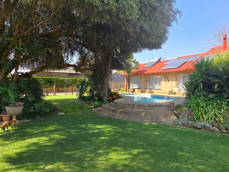 A well-maintained rear garden featuring a swimming pool, mature trees, and solar panels installed on the roof of the main dwelling.