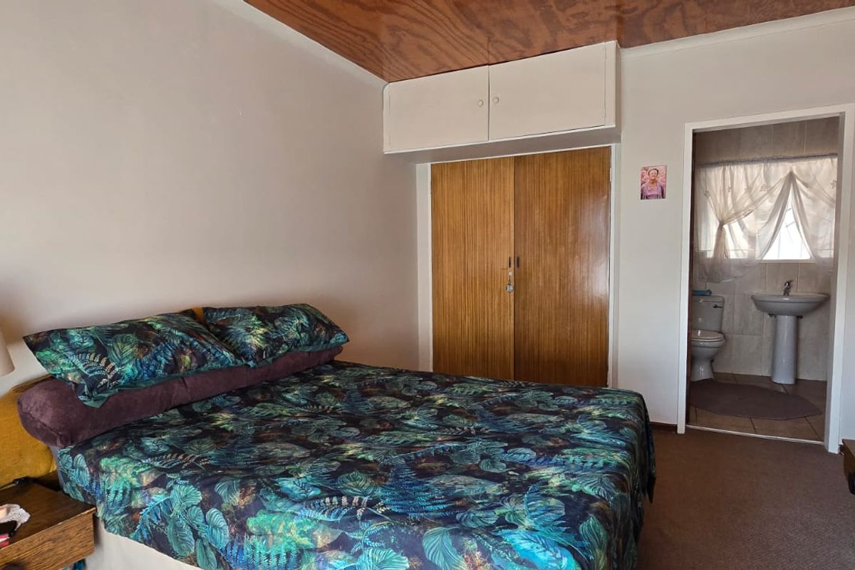 Bedroom featuring built-in wooden wardrobes with overhead storage, a wood-paneled ceiling, and an attached en-suite bathroom with a pedestal basin and toilet.