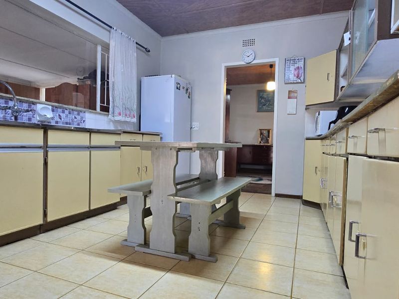 A dated kitchen featuring original cabinetry, tiled flooring, and a functional layout with a pass-through window to the adjacent living area.
