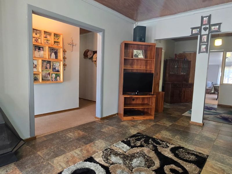 Living room featuring tiled flooring, a freestanding fireplace, and timber ceiling paneling, with open access to adjacent hallway and living areas.
