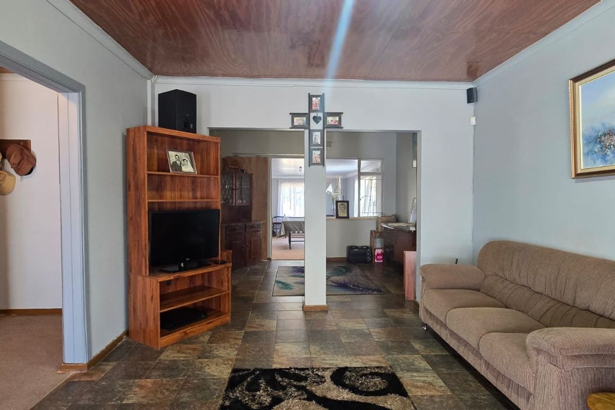 A living room featuring tiled flooring and a wood-paneled ceiling, with an open-plan layout leading into adjacent living spaces.