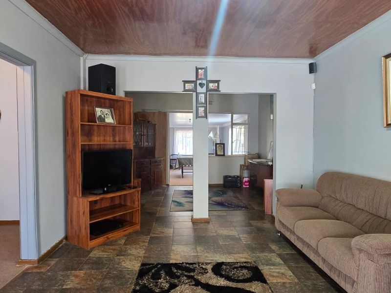 A living room featuring tiled flooring and a wood-paneled ceiling, with an open-plan layout leading into adjacent living spaces.