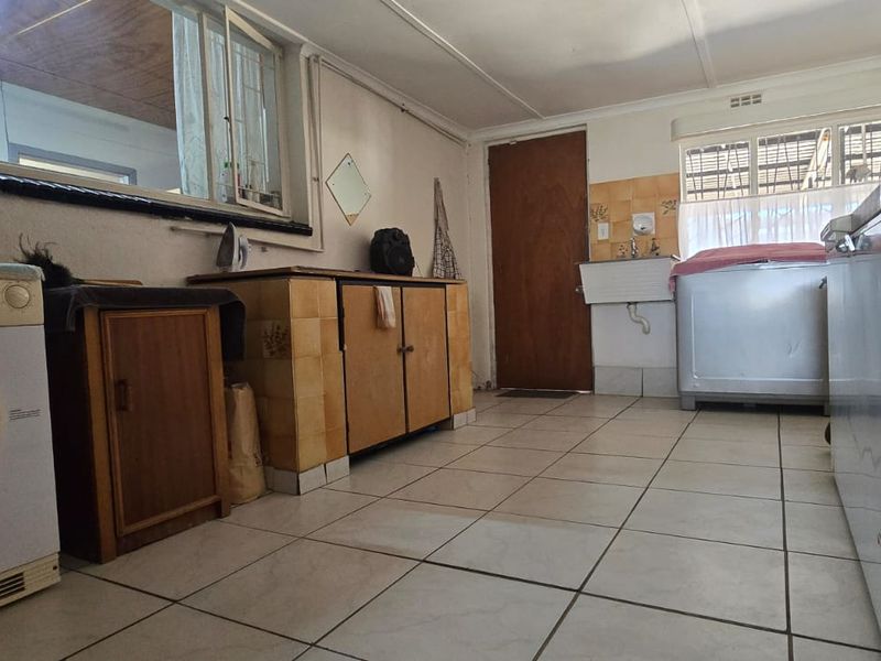 A functional laundry room featuring tiled flooring, a wall-mounted sink, and built-in cabinetry with a tiled splashback.