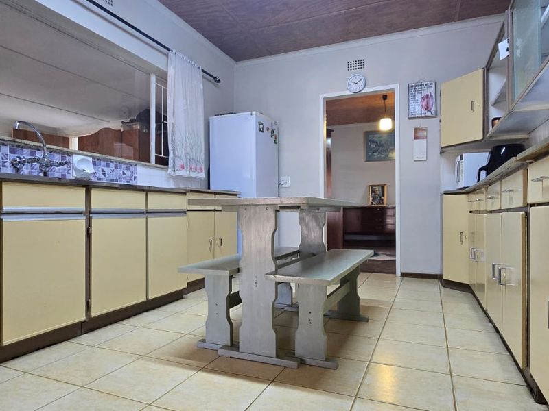 A dated kitchen featuring original cabinetry, tiled flooring, and a functional layout with a pass-through window to the adjacent living area.