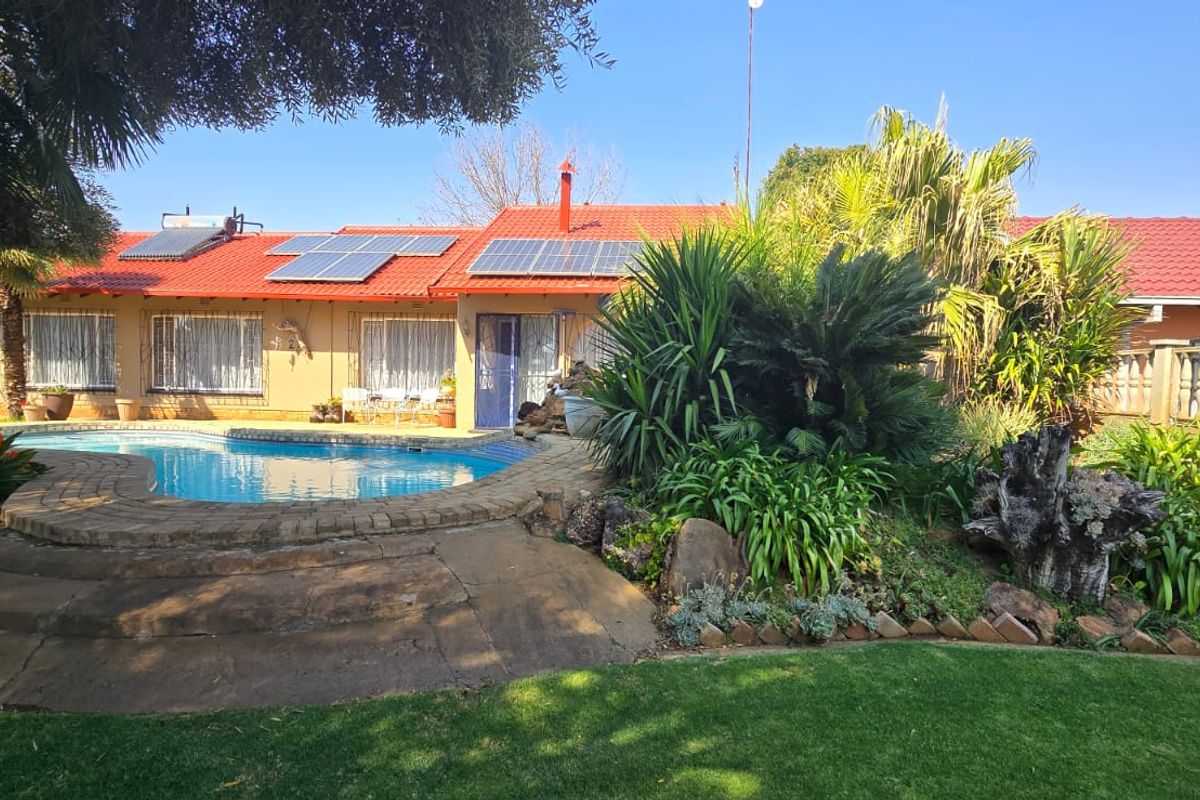 Rear exterior view featuring a swimming pool, landscaped garden, solar panels, and a tiled roof house facade.