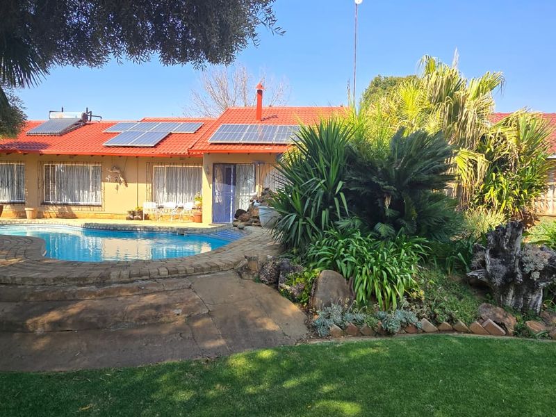 Rear exterior view featuring a swimming pool, landscaped garden, solar panels, and a tiled roof house facade.