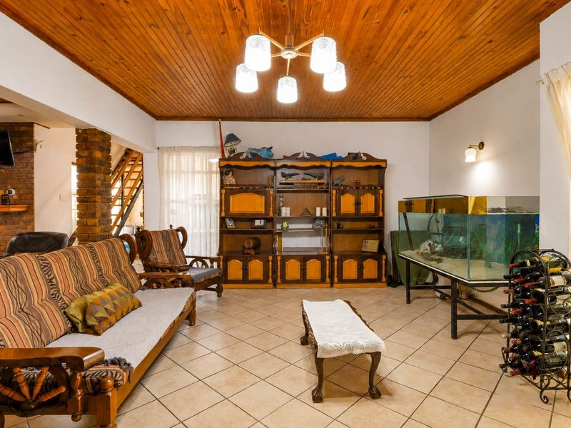 Spacious living room featuring a warm timber tongue and groove ceiling, ceramic tiled flooring, and an exposed brick pillar leading to the staircase.
