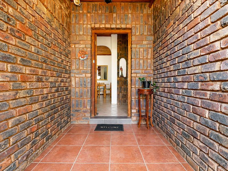 A covered entrance featuring rustic exposed brick walls and tiled flooring, leading into the main living area of the home.