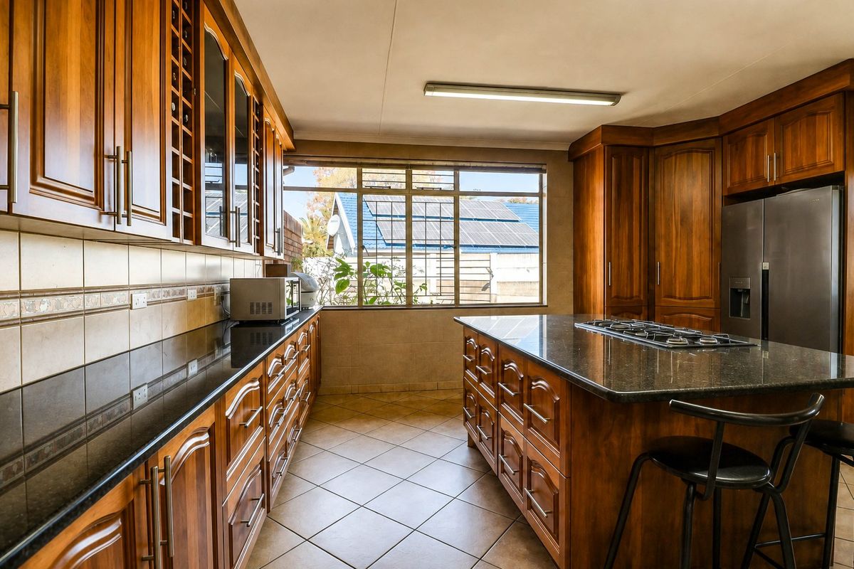 A well-maintained kitchen featuring warm wooden cabinetry, granite countertops, a central island with a gas hob, and tiled flooring.