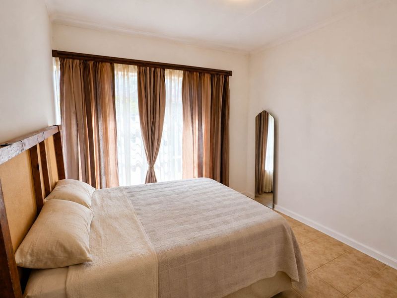 A simple bedroom featuring tiled flooring and a large window with installed curtain rods, providing a neutral base for interior design.