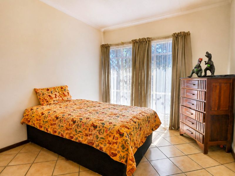 A bedroom featuring tiled flooring and large windows with curtain rails, providing natural light.