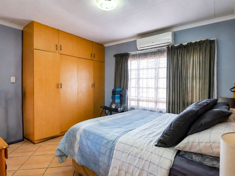 A bedroom featuring built-in wooden cupboards, tiled flooring, and a wall-mounted air conditioning unit.