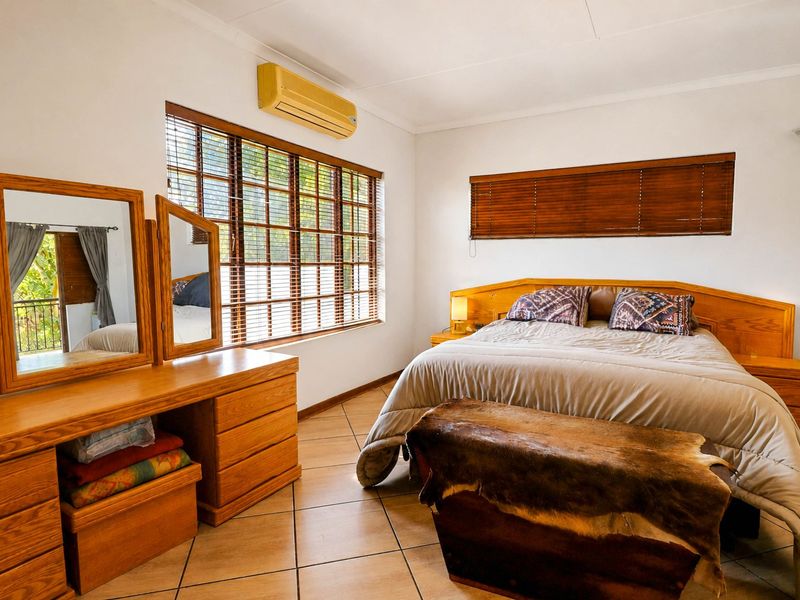 A well-lit bedroom featuring tiled flooring, wooden blinds, and a wall-mounted air conditioning unit.