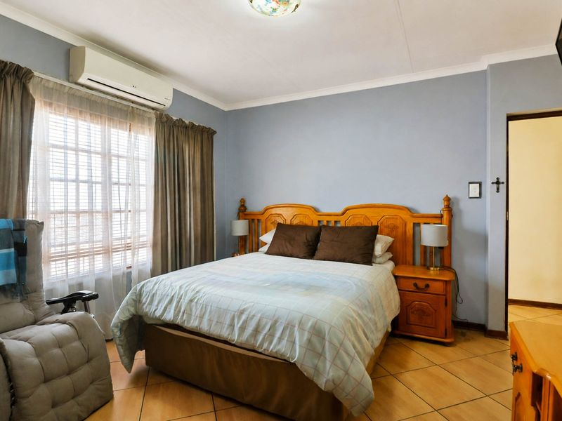 A well-maintained bedroom featuring tiled flooring, a split-system air conditioner, and a window with security bars.