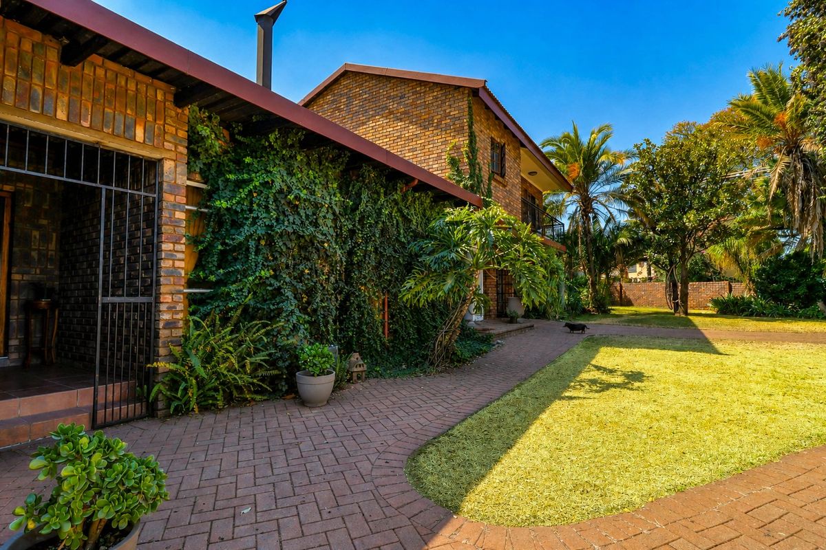 A rear view of a face brick house featuring a paved walkway, established garden, and a covered patio area with security gate.