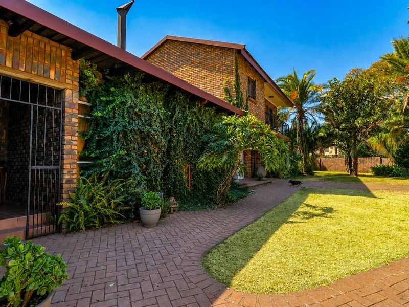 A rear view of a face brick house featuring a paved walkway, established garden, and a covered patio area with security gate.