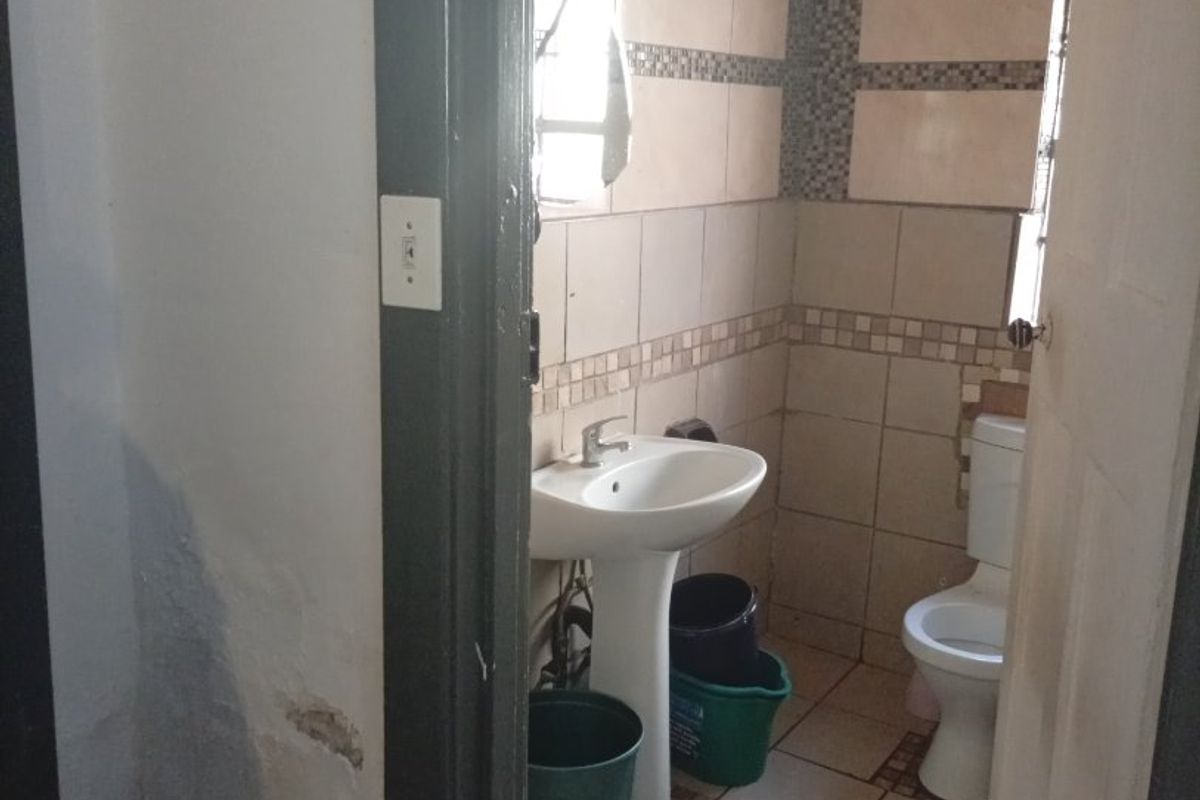 A small bathroom featuring a pedestal basin and toilet with tiled walls and flooring, currently showing signs of wear and maintenance requirements.