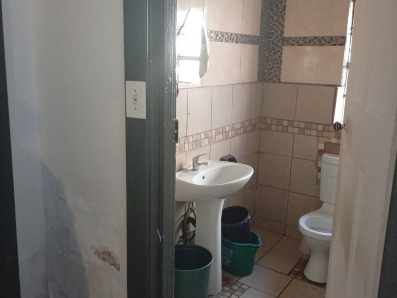 A small bathroom featuring a pedestal basin and toilet with tiled walls and flooring, currently showing signs of wear and maintenance requirements.