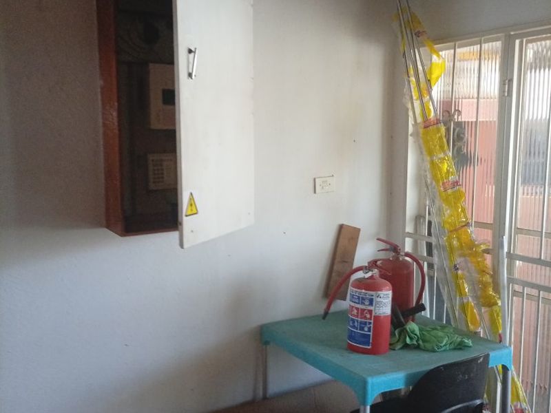 A utility space featuring an exposed electrical distribution board and a security gate, currently used for storage.