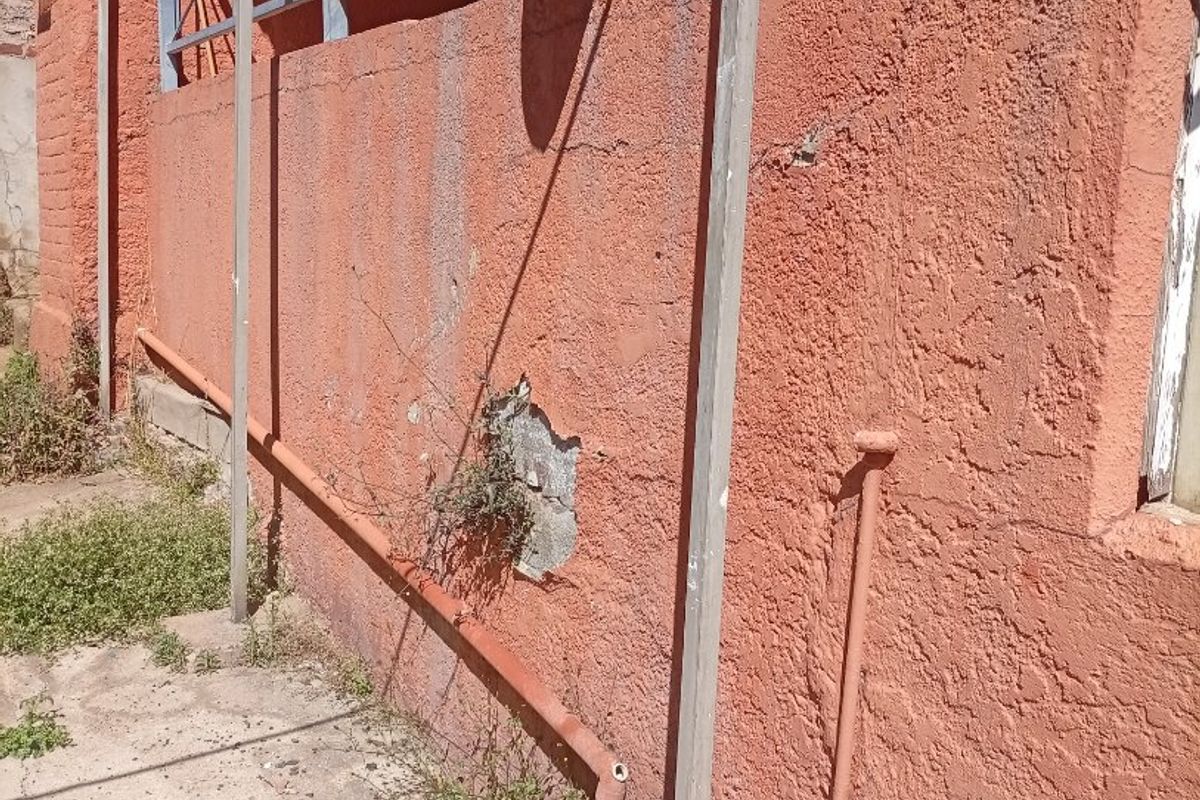 Rear exterior wall showing significant plaster damage, exposed brickwork, and weathered metal support structures with associated drainage infrastructure.