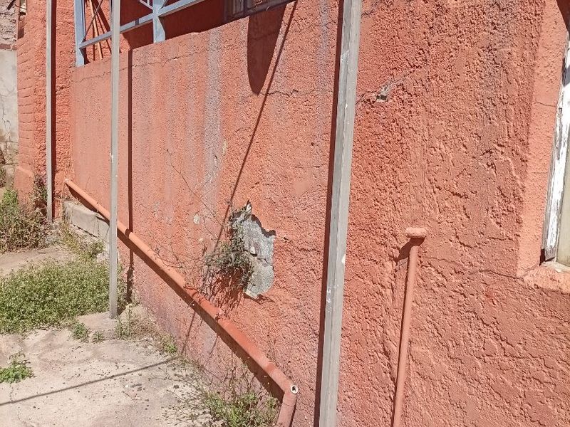 Rear exterior wall showing significant plaster damage, exposed brickwork, and weathered metal support structures with associated drainage infrastructure.