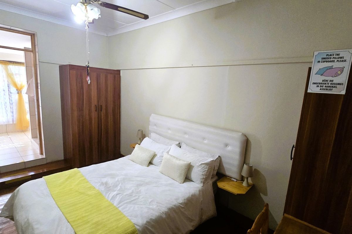 A bedroom featuring wooden flooring, a ceiling fan, and built-in wardrobe storage, with an adjoining room visible through the doorway.