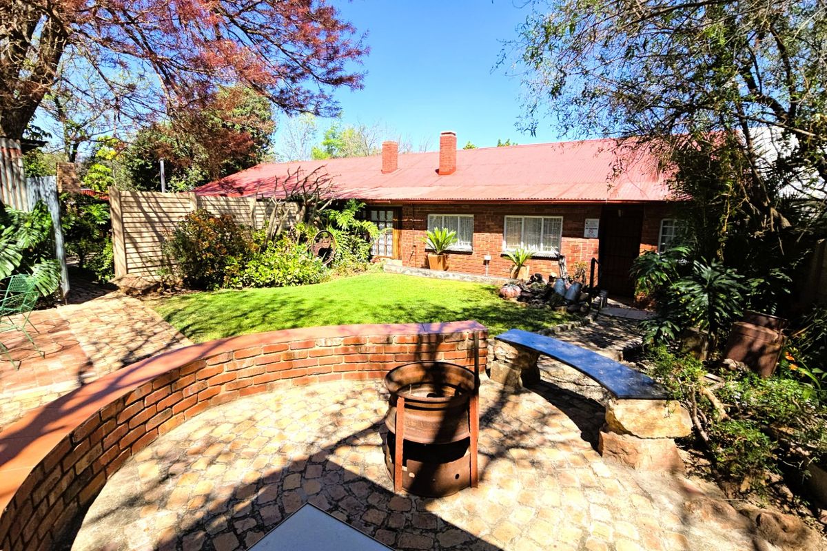 Rear view of the property featuring a brick facade, corrugated metal roof, and a paved patio area with a built-in brick retaining wall.
