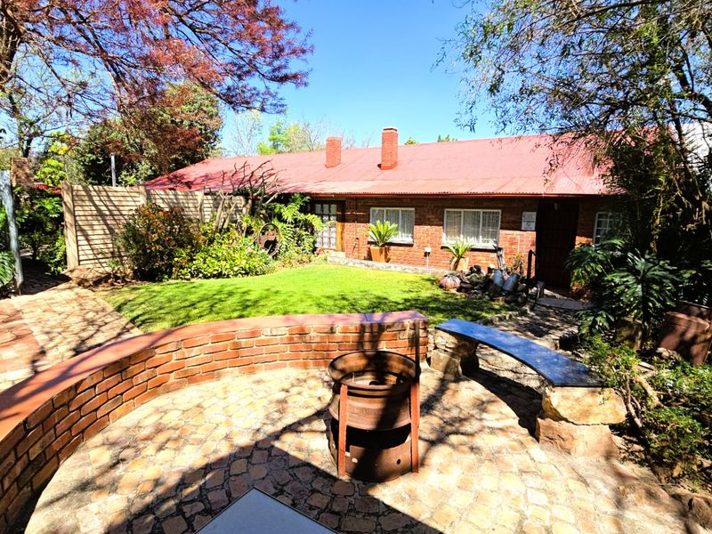 Rear view of the property featuring a brick facade, corrugated metal roof, and a paved patio area with a built-in brick retaining wall.
