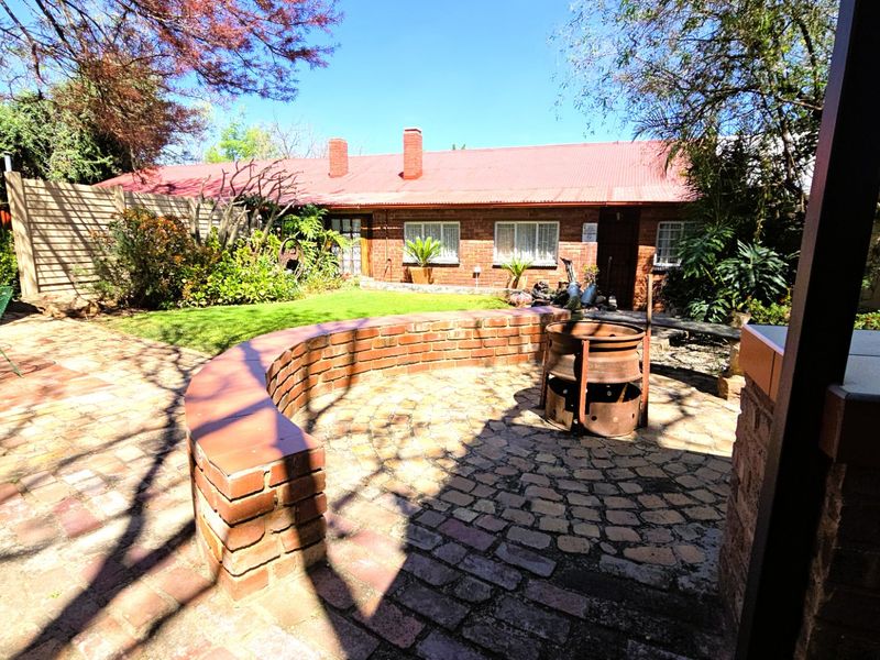A rear garden area featuring a brick-paved patio with a curved brick wall, lawn, and a view of the brick house exterior.