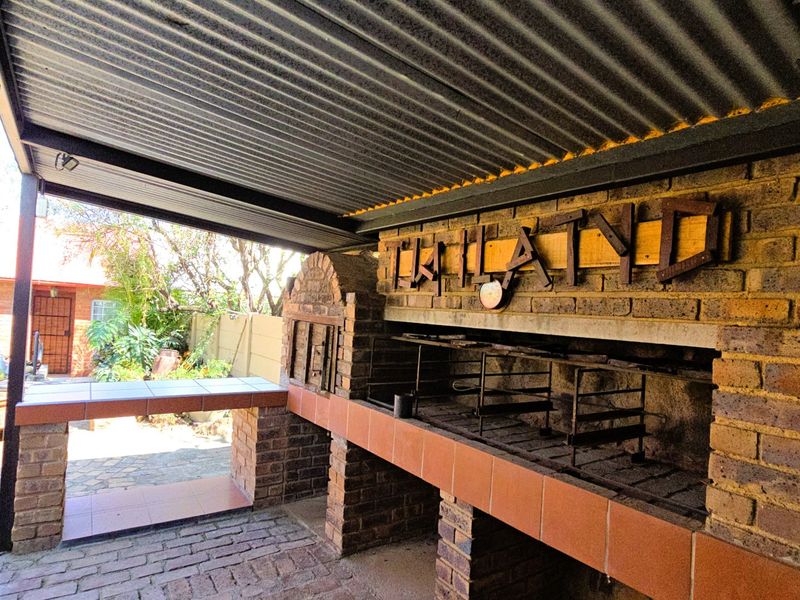 Covered outdoor patio featuring a large built-in brick braai area with tiled prep surfaces and corrugated metal roofing.